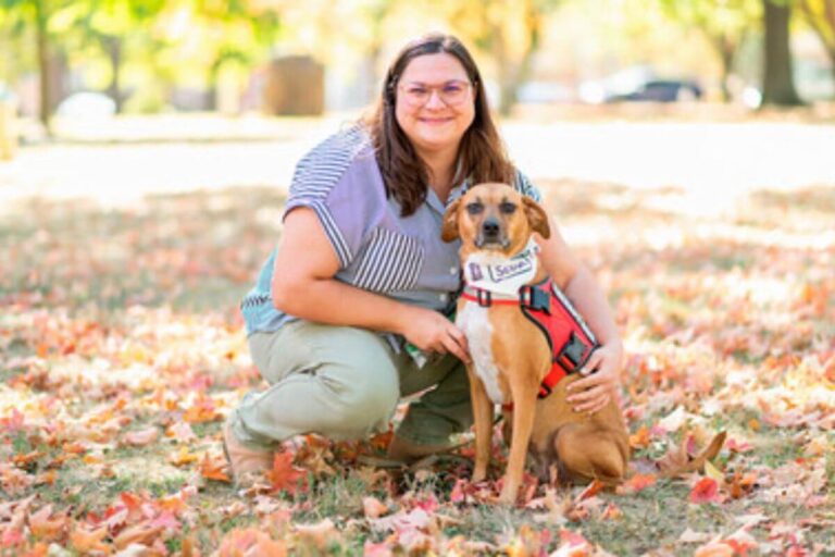Un chien thérapeutique interagit avec une étudiante assise sur l’herbe, créant une atmosphère apaisante et montrant l’importance des animaux dans la gestion de l’anxiété étudiante.
