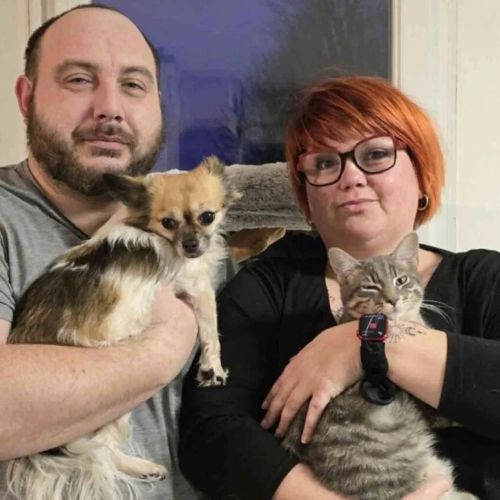 Lilly Labarre, souriante, tenant un petit chien dans ses bras, accompagnée de son mari, symbole de résilience et de passion pour les animaux.