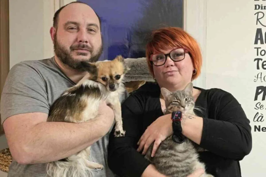 Lilly Labarre, souriante, tenant un petit chien dans ses bras, accompagnée de son mari, symbole de résilience et de passion pour les animaux.