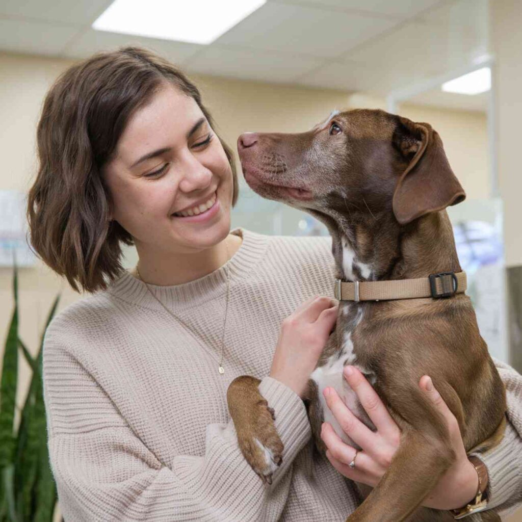 Une femme souriante tient un chien dans ses bras, illustrant le lien affectif entre un adoptant et son futur compagnon.