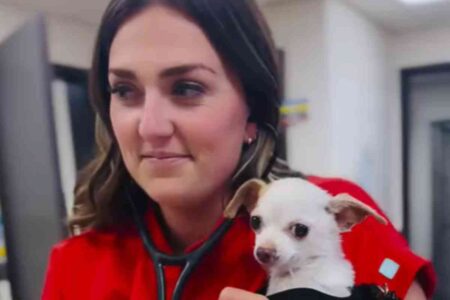Une vétérinaire en blouse rouge tenant un petit chien blanc, souriante, illustrant son talent pour imiter les comportements canins.