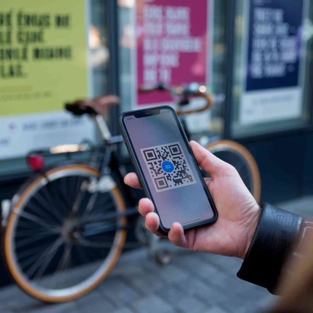 Main tenant un smartphone affichant un QR code devant un vélo