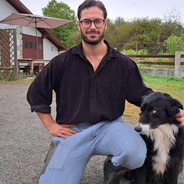 Alexandre, fermier des Landes sélectionné pour Mister Univers 2025, pose devant sa ferme avec son chien.