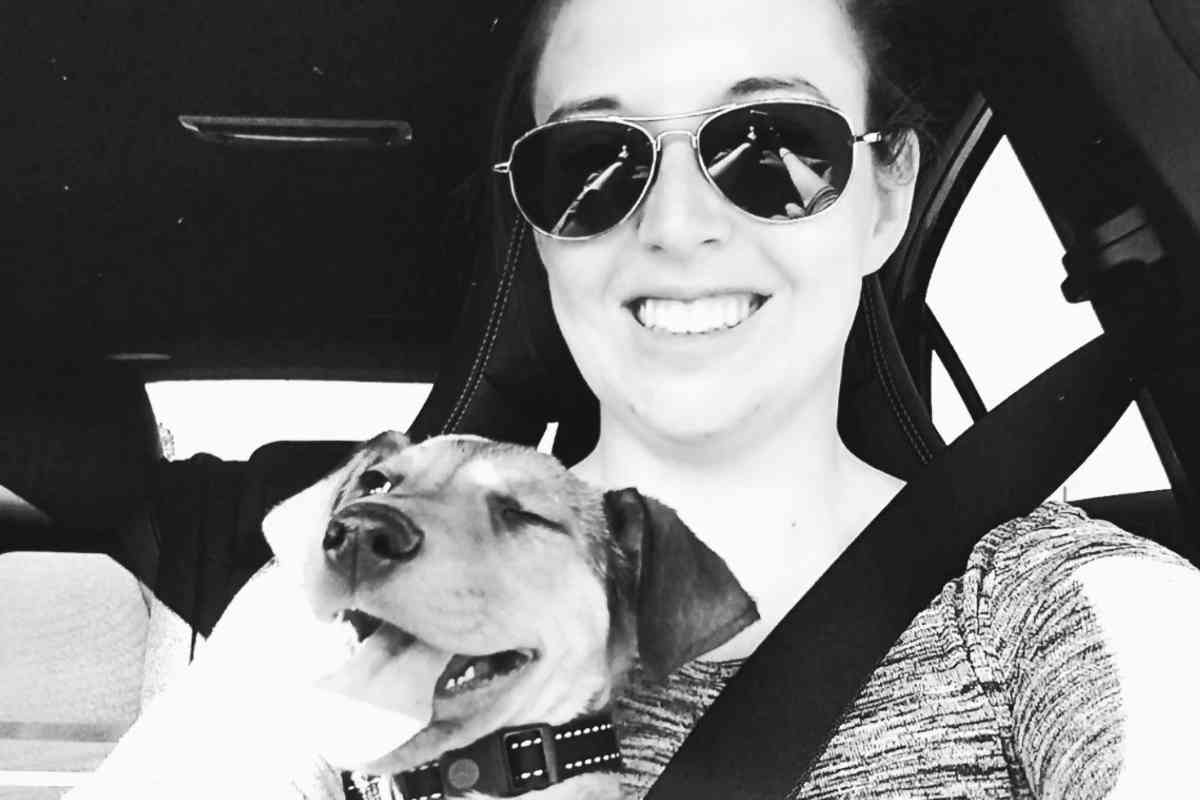 Camille souriante dans une voiture, tenant son chien heureux contre elle.