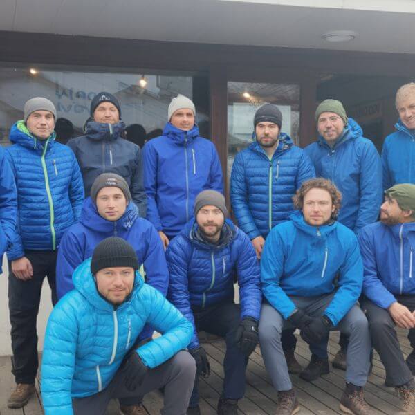 Chiens d’avalanche : ces héros silencieux qui veillent sur la montagne 1 Illustration d’un groupe de maîtres-chiens d’avalanche et de leurs chiens réunis avant la saison hivernale, symbolisant la préparation et l’esprit d’équipe – Crédit photo : Planipets Média