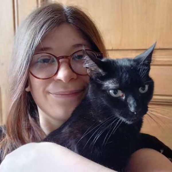Personne souriante portant des lunettes, tenant un chat noir dans ses bras.