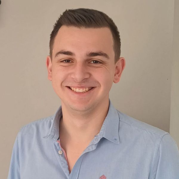 Personne souriante portant une chemise claire, posant devant un fond neutre.